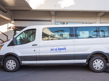 A white van with the logo "Maui Beach Hotel" is parked outside a building. It appears to be a shuttle service vehicle.