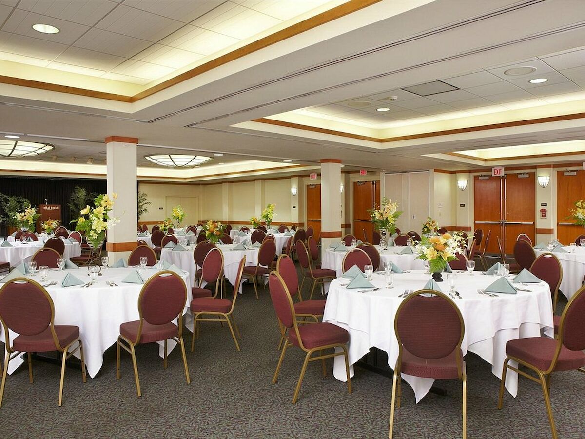 A banquet hall with round tables covered in white cloth, set with napkins, chairs, and floral centerpieces, ready for an event or gathering.