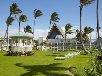A lush lawn with palm trees, a gazebo, and white lounge chairs is surrounded by buildings under a clear blue sky.