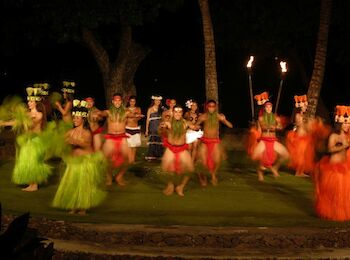 People in colorful traditional outfits are performing a dance at night, with some holding torches.