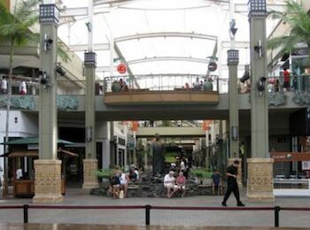 The image shows a shopping mall with multiple people sitting and walking around, featuring stores, open spaces, and decorative pillars.