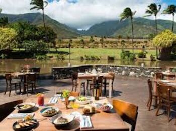 This image depicts an outdoor restaurant setting with tables and chairs, food on the tables, and a scenic mountainous background with lush greenery.